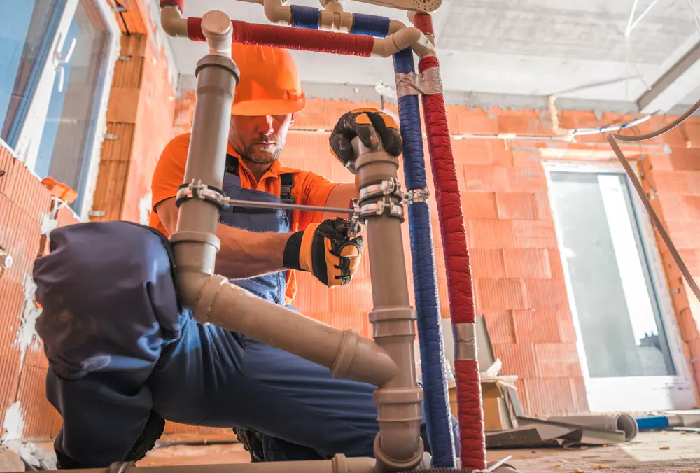 Plumber installing supply and drain rough-in inside the framing of a new house