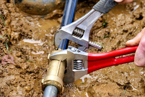Plumber shutting off the water supply and inspecting a burst pipe in a flooded residential basement