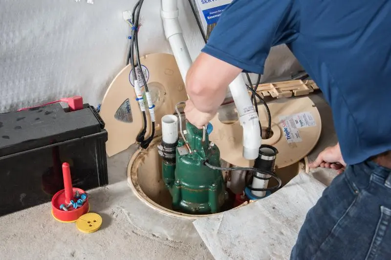 Close-up of a technician replacing a sump pump float switch in a basement pit